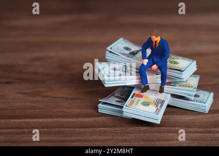 Spielzeugfigur eines Geschäftsmannes, der auf Geldstapeln sitzt und finanzielle Erfolge und Strategien zur Vermögensverwaltung symbolisiert. Stockfoto