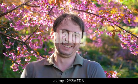 Mann lächelt und entspannt unter blühenden Kirschblüten in sonniger Sonne Stockfoto