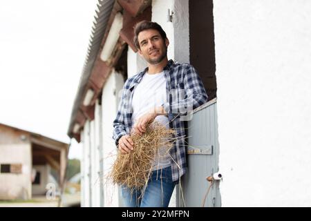 Hübscher Cowboy, der sich auf der Ranch an die Wand lehnt Stockfoto