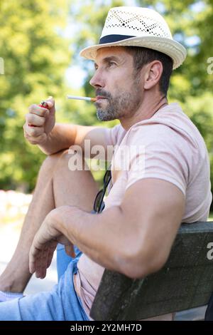 Der Mann saß auf der Parkbank und zündete eine Zigarette an Stockfoto