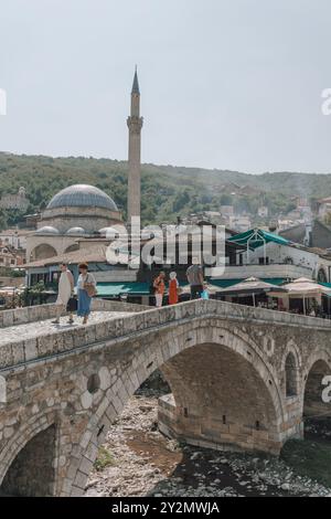 Touristen und Einheimische auf der Alten Steinbrücke über den Fluss Bistrica im Zentrum von Prizren im Kosovo, mit dem Minarett der Sinan Pascha Moschee dahinter. Stockfoto