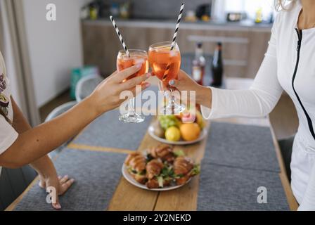 Zwei Gläser mit Cocktails vor einem Holztisch mit Essen und Obst. Die Party beginnt Stockfoto
