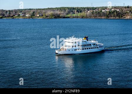 Passagierschiff durch den Stockholmer Archipel in der Ostsee mit traditionellen weißen und roten Häusern in der sonnigen Frühlingsabendlandschaft. Stockfoto