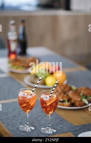 Zwei Gläser mit Cocktails vor einem Holztisch mit Essen und Obst. Die Party beginnt Stockfoto