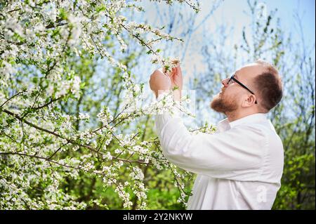 Mann-Allergie genießt nach Behandlung von Saisonallergie im Frühjahr. Porträt eines glücklichen bärtigen Mannes, der im Frühling vor einem Blütenbaum lächelt. Frühjahrsallergiekonzept. Stockfoto