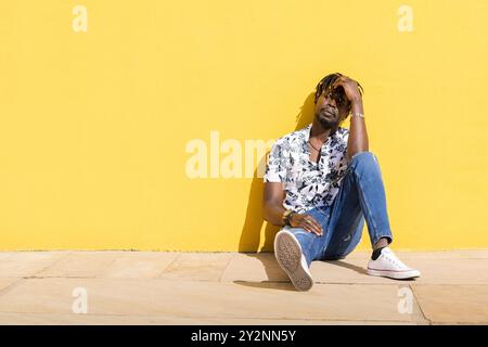 Schwarzer Mann, der auf dem Boden an der gelben Wand sitzt Stockfoto