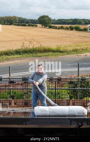 Frau, die Solarpaneele auf dem Dach eines Norfolk-Landhauses reinigt. NB: Die Räumlichkeiten auf dem Foto sind freigegebenes Eigentum. Stockfoto