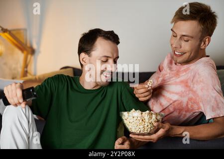 Zwei Männer teilen sich einen freudigen Moment mit Popcorn, während sie zu Hause einen Film sehen. Stockfoto