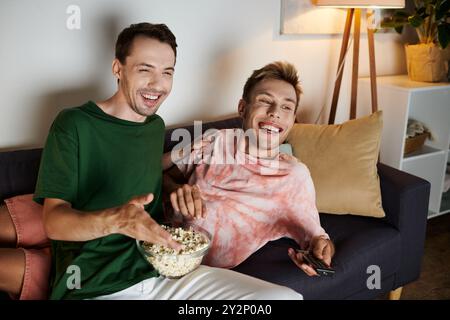 Zwei Männer teilen freudige Momente auf der Couch, während sie Popcorn essen. Stockfoto