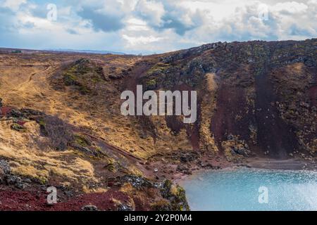 Ein ruhiger Blick auf den Kerid-Krater, eine vulkanische Caldera in Island. Der tiefblau-grüne See bildet einen wunderschönen Kontrast zum roten vulkanischen Felsen und dem üppigen Grün Stockfoto