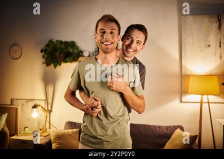 Zwei Männer teilen sich einen freudigen Moment, während sie sich in ihrem Wohnzimmer umarmen. Stockfoto