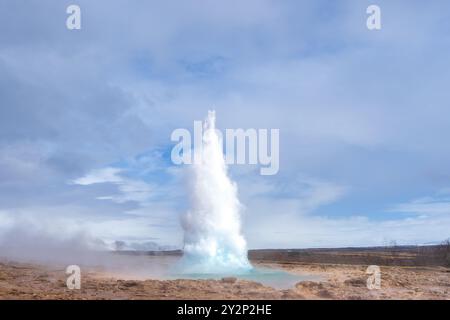 Touristen bestaunen den Strokkur Geysir, der eine Wolke Dampf und Wasser hoch in die Luft schickt. Dieses geothermische Wunder ist eine beliebte Attraktion Stockfoto