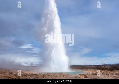 Touristen bestaunen den Strokkur Geysir, der eine Wolke Dampf und Wasser hoch in die Luft schickt. Dieses geothermische Wunder ist eine beliebte Attraktion Stockfoto