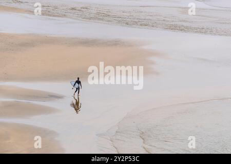 Ein einsamer Surfer mit seinem Surfbrett geht am Crantock Beach bei Ebbe an der Küste von Newquay in Cornwall in Großbritannien, Europa. Stockfoto