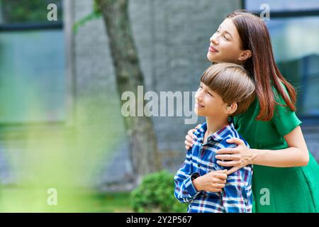 Eine liebevolle Mutter umarmt ihren fröhlichen Sohn in einem üppigen Garten. Stockfoto