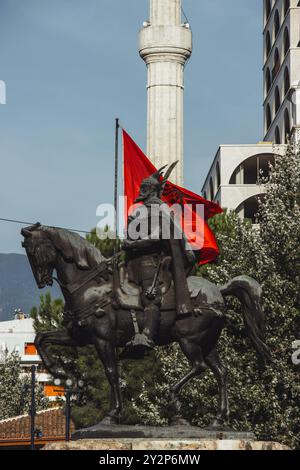 Die Statue von Skanderbeg, die auf einem Pferd reitet, mit der albanischen Flagge und dem Minarett einer Moschee im Hintergrund. Die Statue steht auf dem Skanderbeg-Platz. Stockfoto