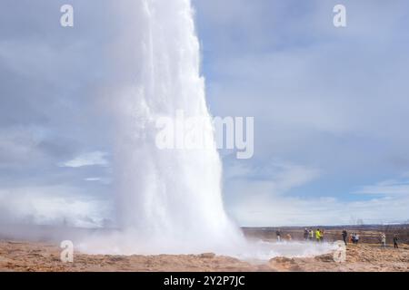 Geysir Geothermiegebiet, Island - 6. Mai 2024: Touristen bestaunen den Strokkur Geysir, der eine Wolke aus Dampf und Wasser hoch in die Luft schickt. Stockfoto