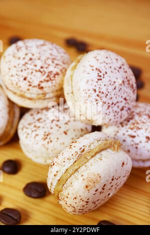 Köstliche Tiramisu Macarons auf hölzernem Hintergrund mit verstreuten Kaffeebohnen Stockfoto