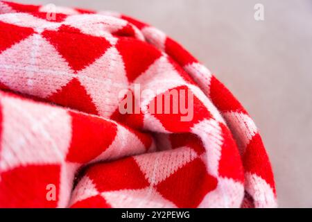 Eine Nahaufnahme aus einem leuchtend rot-weißen karierten Strickmaterial mit klassischem Argyle-Muster. Das strukturierte Material erzeugt ein Gefühl von Wärme und Wärme Stockfoto