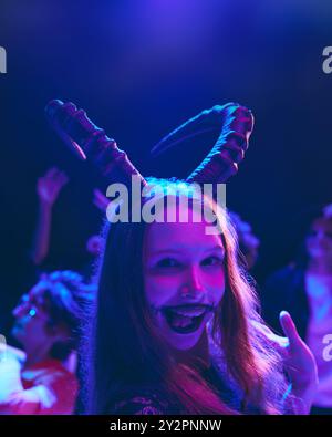 Porträt eines lächelnden jungen Mädchens mit gruseligem Make-up und Tierhörnern auf dem Kopf, das Halloween mit Freunden im Nachtclub feiert. Stockfoto