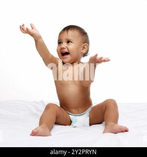 Glückliches kleines Mädchen, Kind in Windel, das auf dem Bett sitzt und fröhlich, Hände klatschend in Freude und Spaß isoliert auf weißem Studio Hintergrund Stockfoto