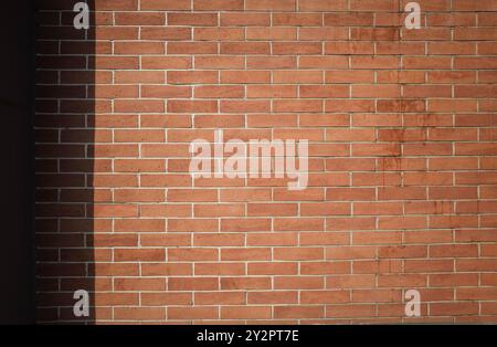 Rote Backsteinmauer Sommerhintergrund mit Schatten. Hintergrund für Kopierraum an der Ziegelwand. Stockfoto