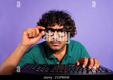 Nahaufnahme eines fokussierten Guy Systemadministrators, der mit pc-Bildschirm-TAP-Tastatur arbeitet, Brillen auf violettem Hintergrund isoliert Stockfoto