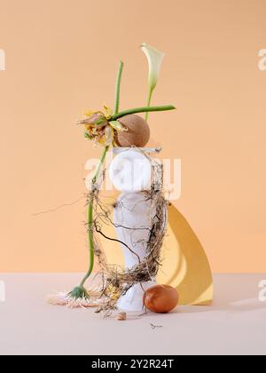 Dieses Bild zeigt ein konzeptionelles Stillleben mit Blumen, einem goldenen Stoff und natürlichen Texturen, die eine künstlerische Komposition auf einem pastellfarbenen Hintergrund schaffen Stockfoto