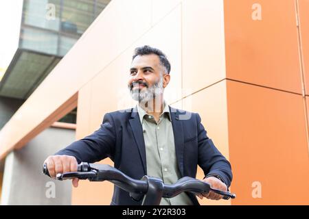 Von unten aus fährt man in formeller Geschäftskleidung mit einem Elektrofahrrad durch die Stadt und bietet eine Mischung aus modernem Transport und professionellem Leben Stockfoto