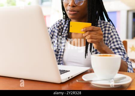 Eine fokussierte schwarze Frau in einem Café im Geschäftsviertel kauft online mit Kreditkarte und Laptop ein. Die Szene fängt einen Moment der modernen Stadt ein Stockfoto