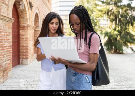Zwei Studenten, die draußen auf einem gepflasterten Weg arbeiten, an einem Projekt auf einem Laptop arbeiten, konzentrieren sich und engagieren sich für ihr Studium Stockfoto