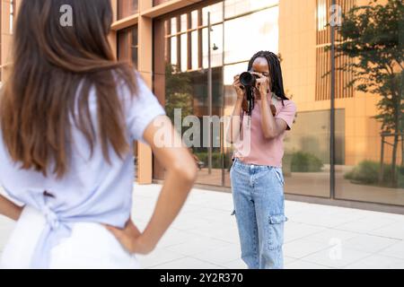 Eine junge afroamerikanische Studentin nimmt mit einer DSLR-Kamera ein Foto ihres Freundes in einer ungezwungenen Universitätsumgebung auf und symbolisiert dabei die Jugend und die Jugend Stockfoto