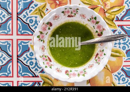 Blick von oben auf eine Schüssel mit traditioneller mexikanischer grüner Salsa, serviert auf einer farbenfrohen Tischdecke mit Blumenmuster und geometrischen Mustern. Das Bild erfasst den vib Stockfoto