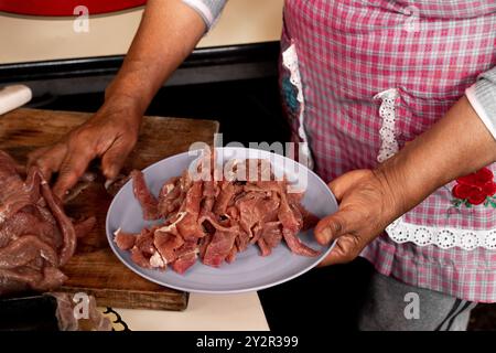 Abgeschnittene, nicht erkennbare Hände einer älteren hispanischen Frau, die in La Marquesa, Mexiko, aufgeschnittenes Fleisch zart in eine Schüssel legt, was die Tradition unterstreicht Stockfoto