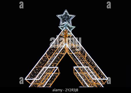 Ein aufwendig gestalteter Weihnachtsbaum, der mit hellen weißen Lichtern und einem leuchtenden Stern gekrönt ist, steht kühn vor einem dunklen Non Stockfoto