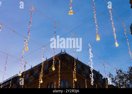 Elegante Weihnachtslichter hängen über einer Straße der Stadt und schaffen eine festliche Atmosphäre vor einem dunkelblauen Himmel. Beleuchtete Figuren unterstreichen das fest Stockfoto