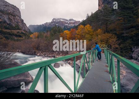 Ein Mann steht auf einer grünen Brücke über dem rauschenden Wasser des Flusses Ara, umgeben von lebhaften Herbstfarben in der Region Ordesa des aragonesischen Pyr Stockfoto