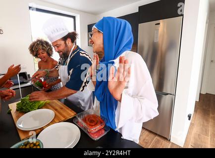 Eine vielfältige Gruppe von Freunden teilt einen freudigen Moment in der Küche, während sie Zutaten für ein Barbecue vorbereiten und eine Mischung aus Kulturen und Teamwork präsentieren Stockfoto