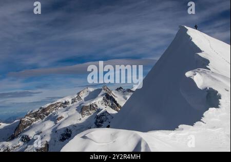 Rückansicht eines nicht erkennbaren Kletterers, der auf dem Gipfel eines schneebedeckten Gipfels in den Schweizer Alpen in der Nähe von Zermatt steht, mit weitläufigem Blick auf die Umgebung Stockfoto