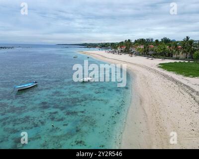 Ein Luftbild, das die ruhige Schönheit eines Sandstrandes auf Mauritius mit kristallklarem Wasser, Booten und einem belebten Strand mit Palmen einfängt Stockfoto