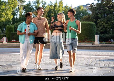 Eine Gruppe von LGBTQIA+ Freunden lacht und Eis, während sie eine sonnige Stadtstraße hinunterlaufen und dabei Vielfalt und Kameradschaft zeigen. Stockfoto