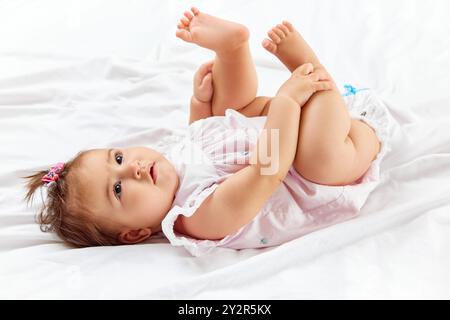 Das charmante Baby spielt fröhlich auf ihrem Rücken und hält ihre winzigen Füße mit Neugier, die vollständig in ihre verspielte Welt verwickelt sind. Stockfoto