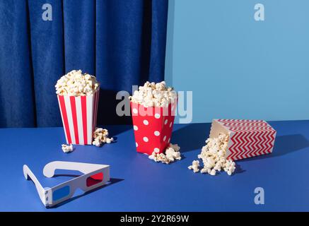 Lebendiges Bild mit drei Eimern Popcorn in rot gestreiften und Punktmotiven, verstreuten Kernen und 3D-Brillen, die gegen eine Gegenüberstellung gestellt werden Stockfoto