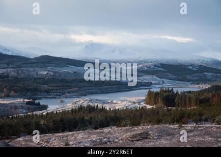 Eine atemberaubende Winterszene aus den schottischen Highlands, die einen ruhigen See zeigt, der von schneebedeckten Bergen und bewaldeten Hügeln umgeben ist, und den q festnimmt Stockfoto