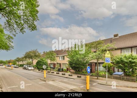 Eine friedliche Vorstadtstraße, gesäumt von Reihenhäusern unter blauem Himmel, mit einem auffälligen Schild für die Schulzone, das eine Geschwindigkeitsbegrenzung von 30 km/h anzeigt. Stockfoto