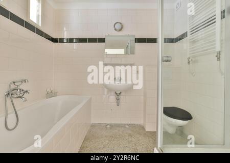 Ein altes gefliestes Badezimmer mit Badewanne, Waschbecken und Toilette mit Fenster für natürliches Licht. Stockfoto