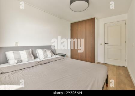 Ein stilvolles, modernes Schlafzimmer mit einem großen Bett mit grauem Kopfteil, strahlend weißer und grauer Bettwäsche und Holzfußboden. Stockfoto