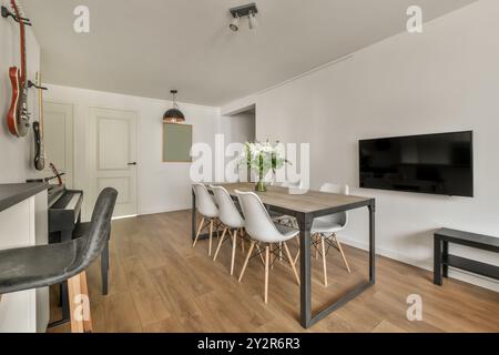 Moderner Essbereich mit Holztisch, weißen Stühlen, Gitarren und Flachbild-TV. Stockfoto