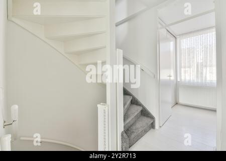 Ein makellos weißes Interieur mit einer modernen Treppe mit grauen Teppichböden, die zu einem oberen Stockwerk führt, neben weißen Wänden und Regalen. Stockfoto