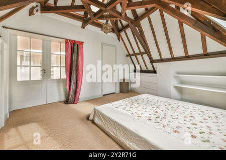 Ein einladendes Schlafzimmer im Dachgeschoss mit freiliegenden Holzbalken, einem komfortablen Doppelbett und einer charmanten Mischung aus modernen und rustikalen Elementen. Stockfoto
